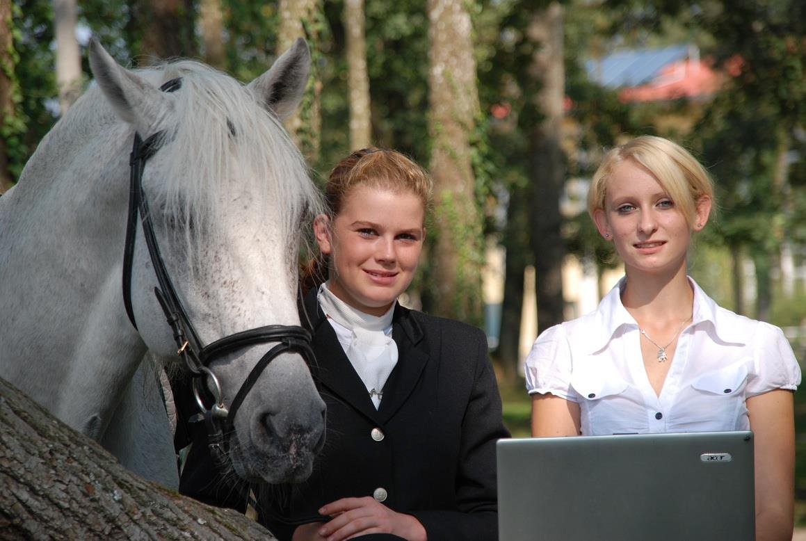 Zwei Schülerinnen mit weißem Pferd und Laptop.